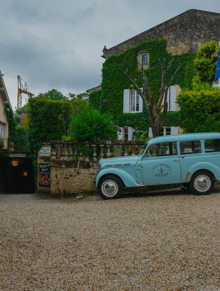A romantic cobblestone square in Saint-Émilion, with historic stone buildings and a vintage car at its center, surrounded by the sounds of the town